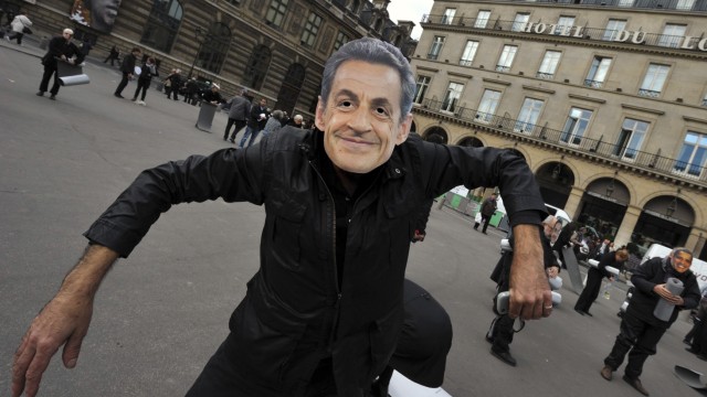An activist wears a mask portraying France's President Sarkozy during a protest at Palais Royal place in Paris