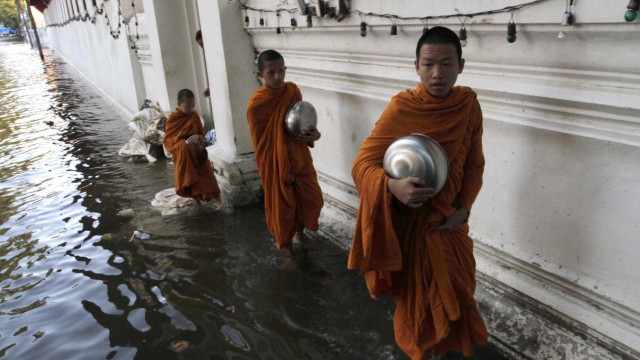 Buddhist monks walk in a flooded street to collect morning alms in Bangkok