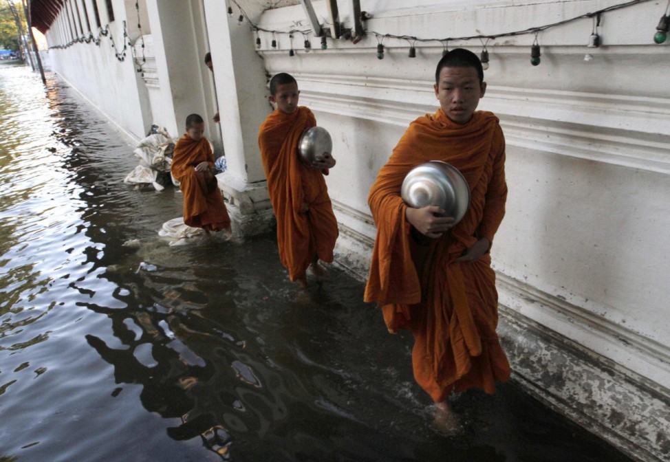 Buddhist monks walk in a flooded street to collect morning alms in Bangkok