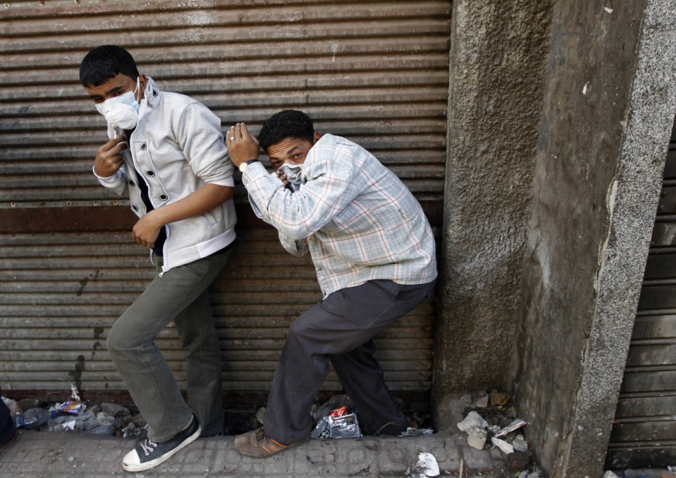 Protesters take cover during clashes with riot police in a side street near Tahrir Square in Cairo