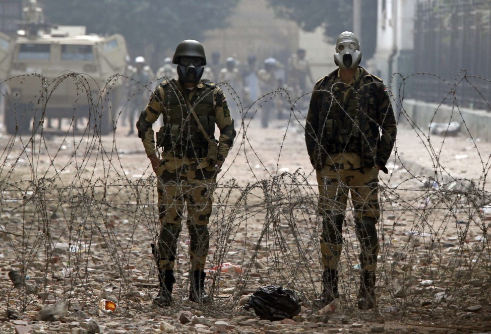 Egyptian army soldiers stand behind a barbed wire barricade during clashes on a side street near Tahrir Square in Cairo