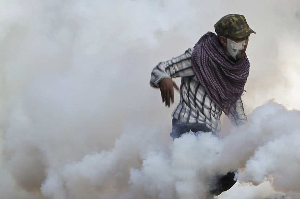 A protester returns a tear gas canister thrown by riot police during clashes near Tahrir Square in Cairo