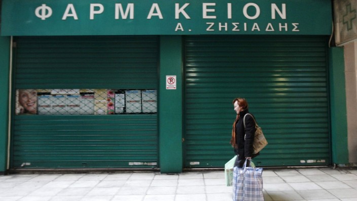 A woman passes in front of a closed pharmacy store during a 48-hour pharmacists strike in Athens