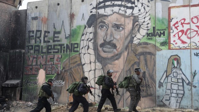 Israeli police and border officers walk in front of a mural depicting Arafat at Qalandiya checkpoint
