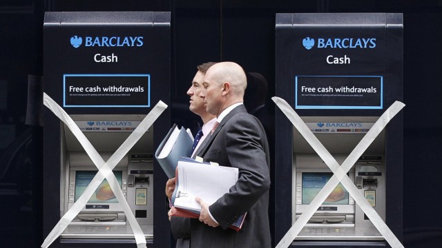 Two men pass closed cashpoints marked with masking tape, outside a Barclays Bank branch being refurbished in City of London