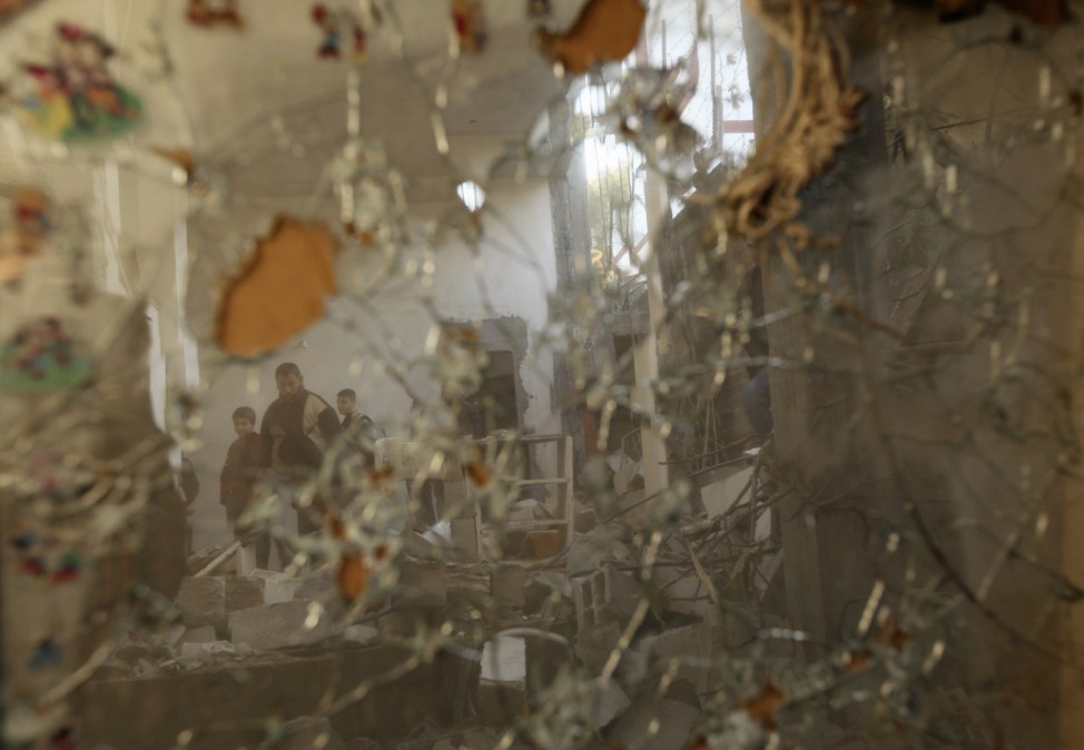 People are reflected in a broken mirror as they walk through a damaged house in the northern Gaza Strip