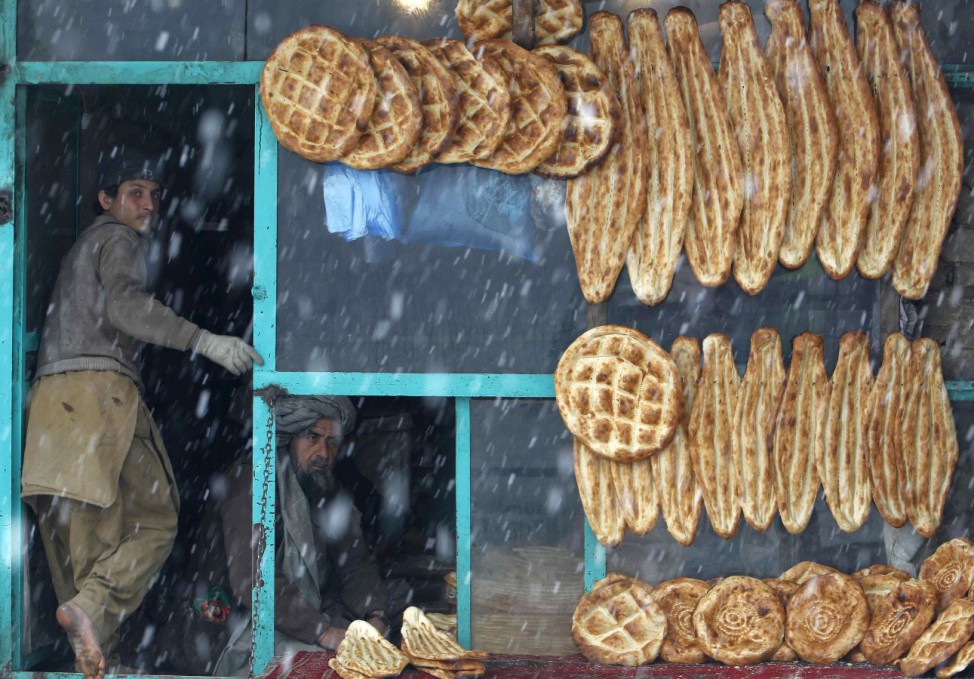 A baker sits at his bakery as he waits for customers on a snowy day in Kabul