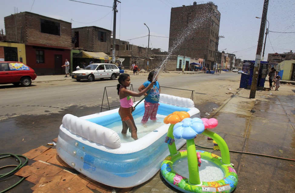 A girl plays with water in an inflatable pool on a street during summer in the southern hemisphere in downtown Lima