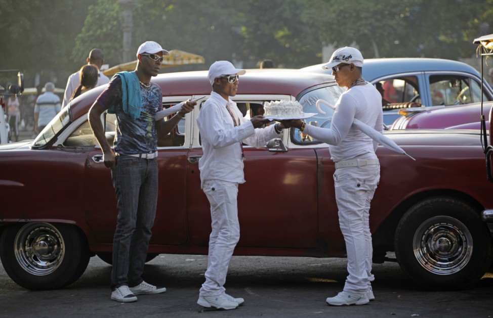 Men carry a cake on the way to an Afro-Cuban religion birthday party beside a taxi in Havana