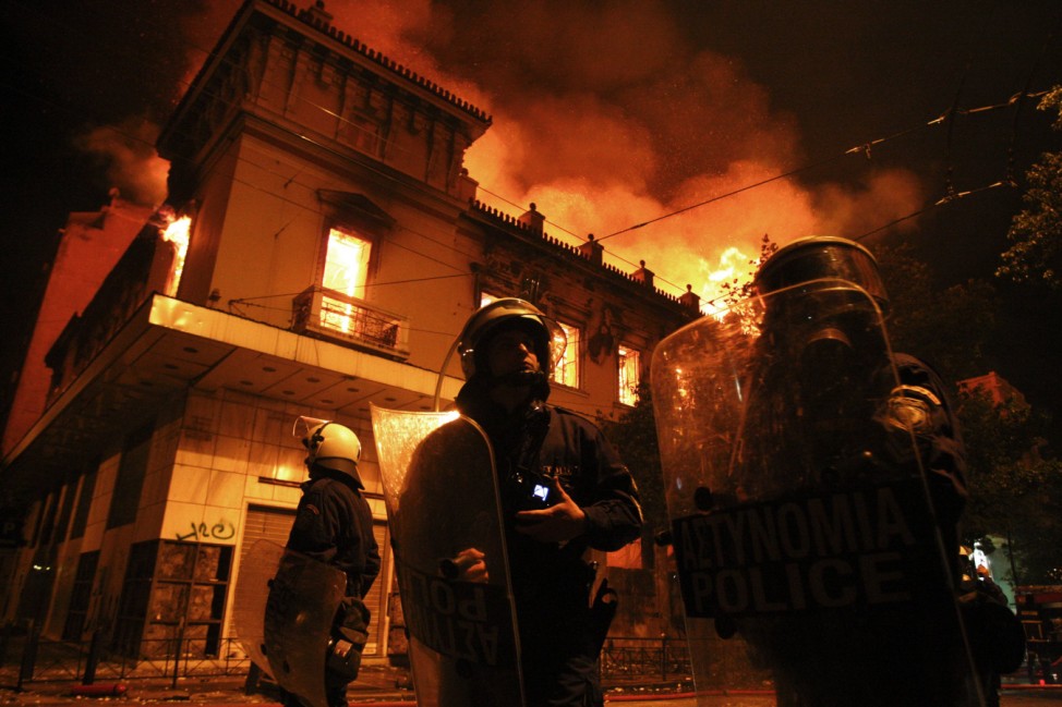 Policemen stand in front of a burning building following violent anti-austerity protests in Athens