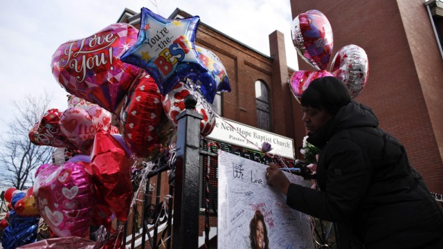 A woman writes a message on a memorial for pop singer Whitney Houston, outside of New Hope Baptist Church in Newark