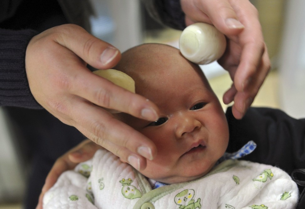 A father gives his baby a head massage with eggs after a haircut at a care center in Hefei