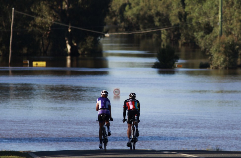 A couple rides near a road submerged in flood waters in Wagga Wagga