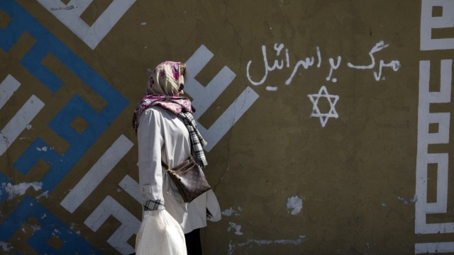 Woman walks past writing on a wall in Persian script that reads, 'Down with Israel', in northern Tehran