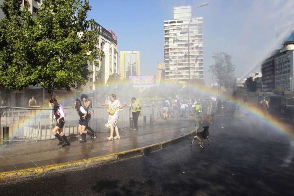 Student protesters and pedestrians run away from jet of water from riot police vehicle during demonstration in Santiago