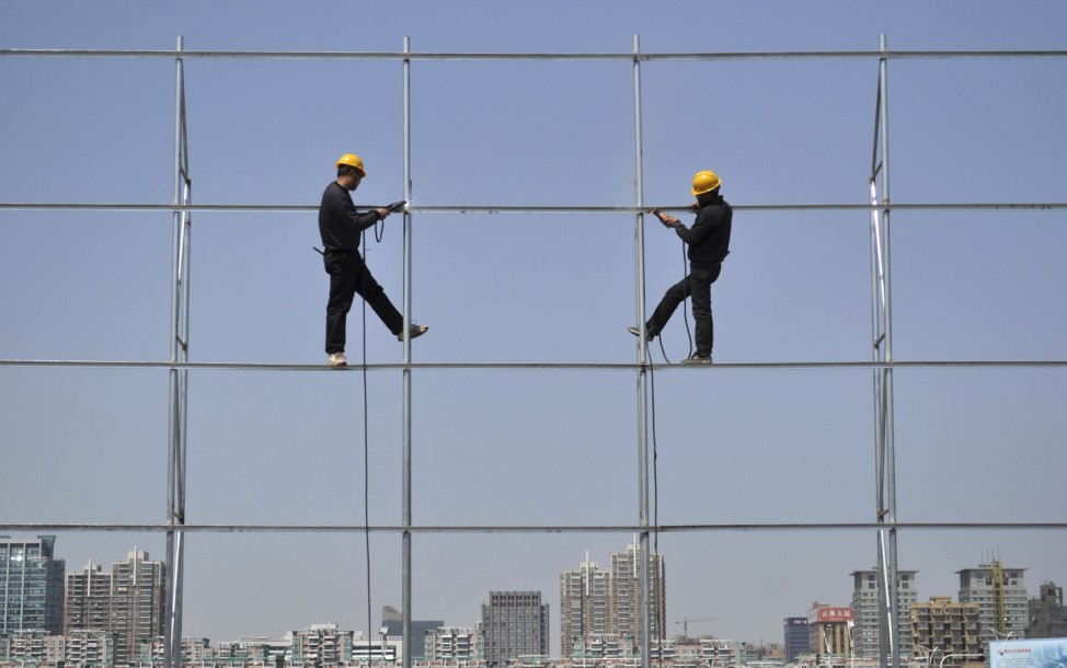 Workers stand on a steel frame which they are welding for an advertising board in Jiaxing