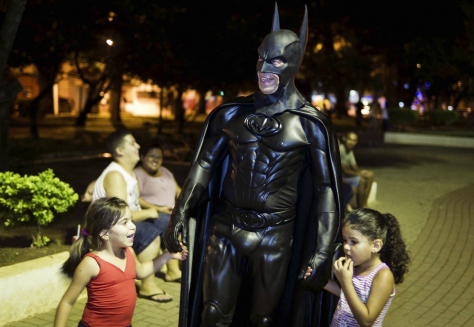 Retired Brazilian police officer Pinheiro, dressed as super-hero Batman, walks with children at Santa Terezinha Square in Taubate city