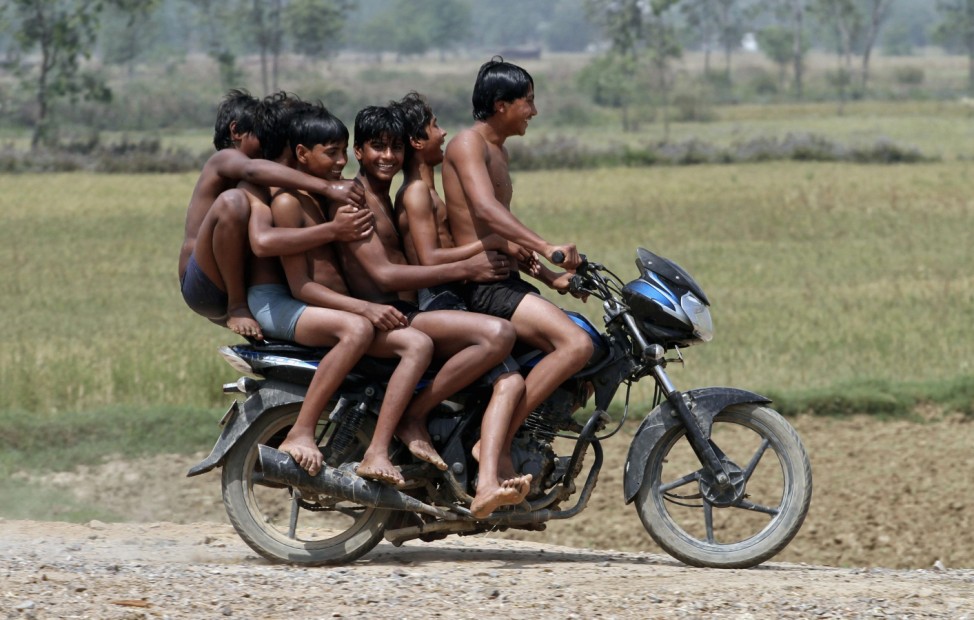 Boys ride a motorbike on their way back home after taking a bath in a canal at Chachura village