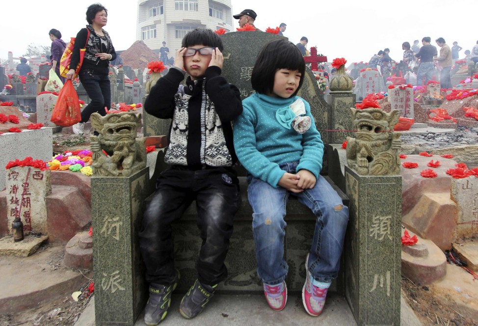 Children sit in front of a tombstone waiting for their relatives at a public cemetery during the Qingming Festival in Jinjiang