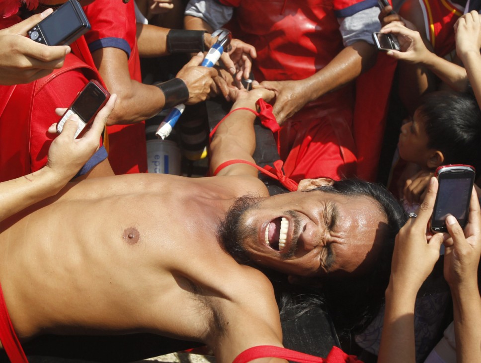 Filipino penitent Bobby Gomez grimaces while being nailed to a wooden cross during a reenactment of Jesus Christ's crucifixion on Good Friday in Barangay Cutud