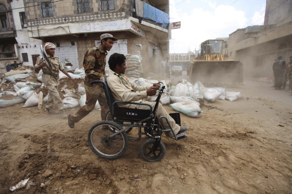 A defected army soldier pushes a disabled person across a street as barricades erected by defected army forces are dismantled in Sanaa