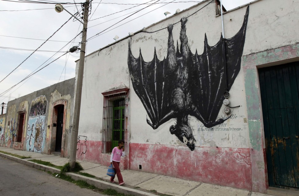 A girl walks on a street beside a wall painted with a mural of a bat in San Pedro Cholula