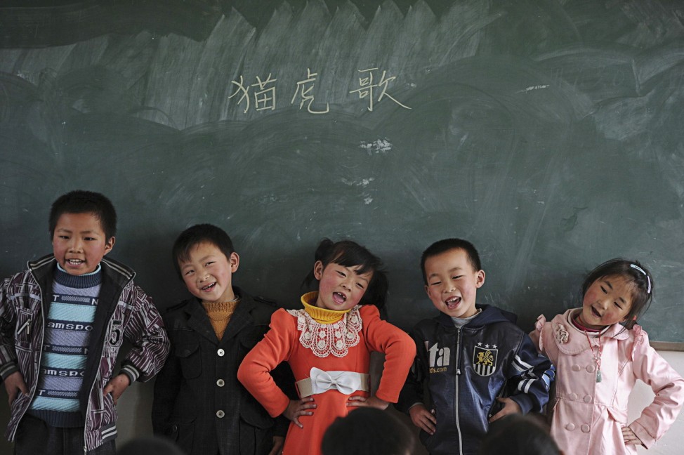 Students stand in front of a black board as they sing a song during class at a primary school in a village in Yuexi county