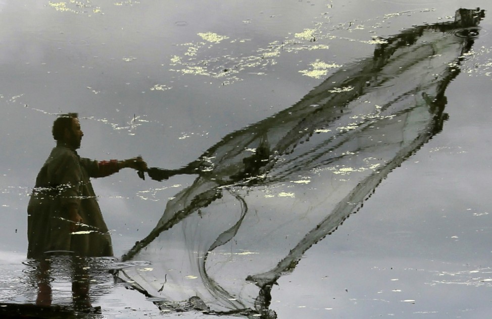 A Kashmiri fisherman is reflected in the waters of Dal Lake as he throws a net to catch fish in Srinagar