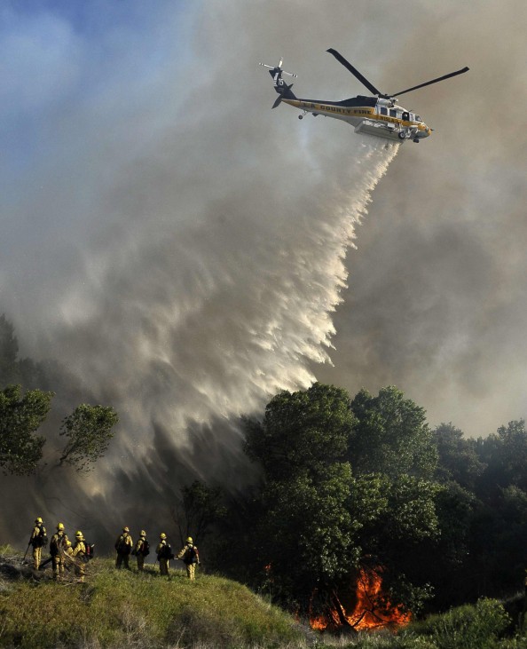 A Los Angeles county helicopter makes a water drop to help firefighters battle a brush fire in Acton, California