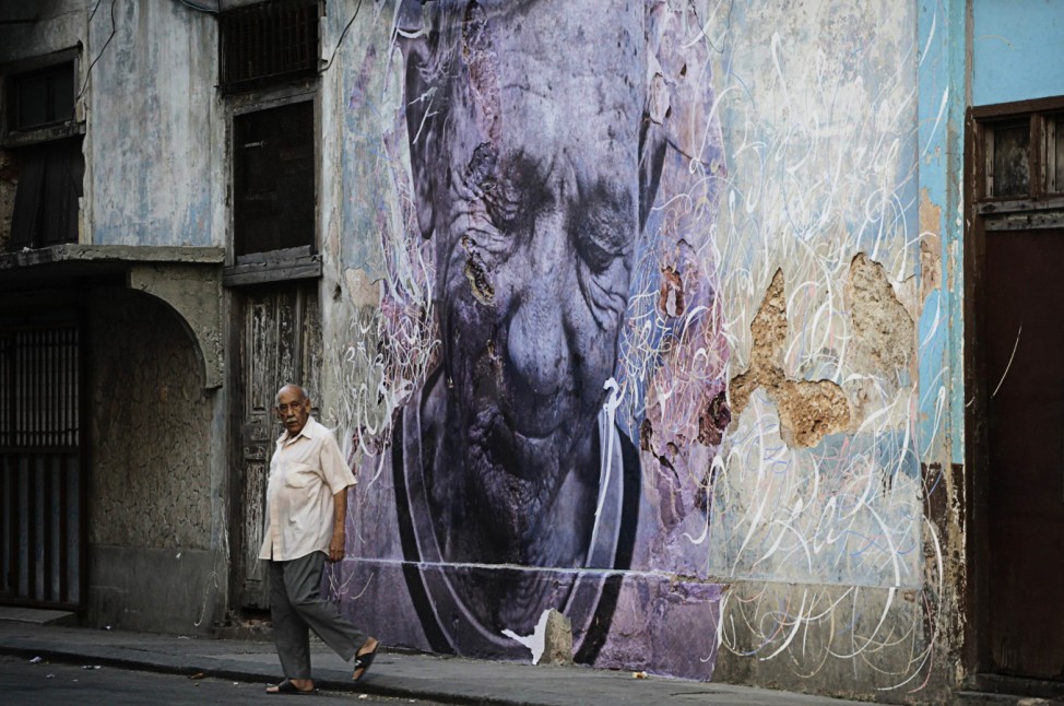 A man walks beside a creation by Cuban-American artist Jose Parla and French artist J.R. on a building wall in Havana