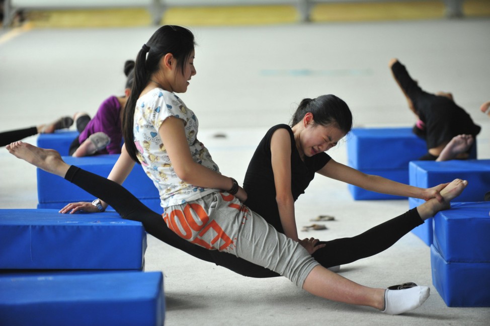A coach sits on a student's leg to help her stretch during a training session at a gymnastic course at Shenyang Sports School in Shenyang
