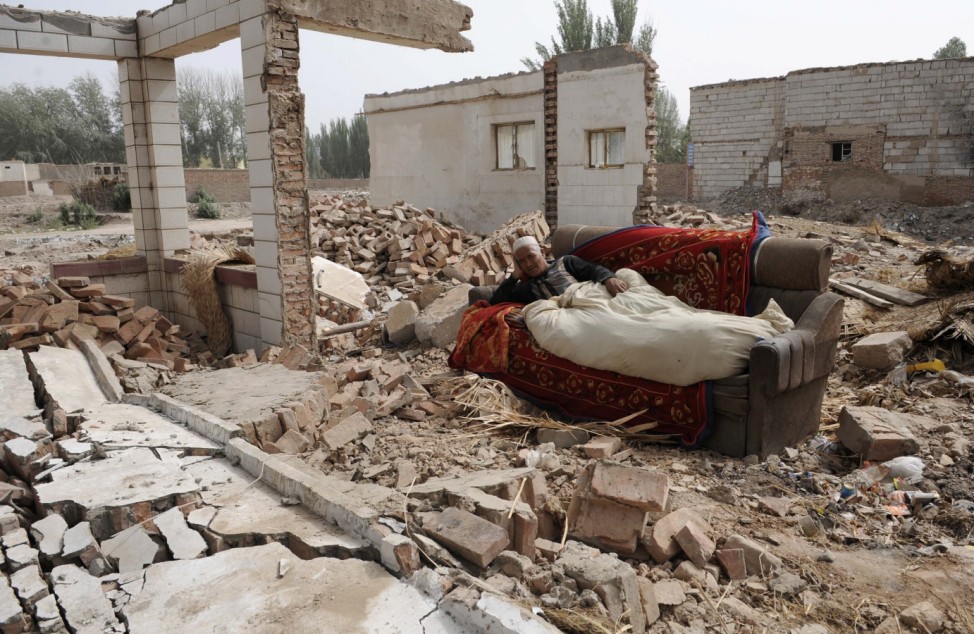 An ethnic Uighur man lies on a couch as he keeps an eye on his belongings at his newly-demolished house making way for a residential complex in Aksu