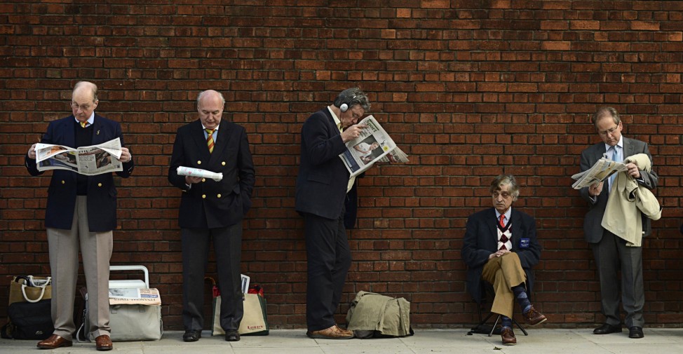 Marylebone Cricket Club members read newspapers as they wait in a queue outside the ground at Lord's cricket ground in London