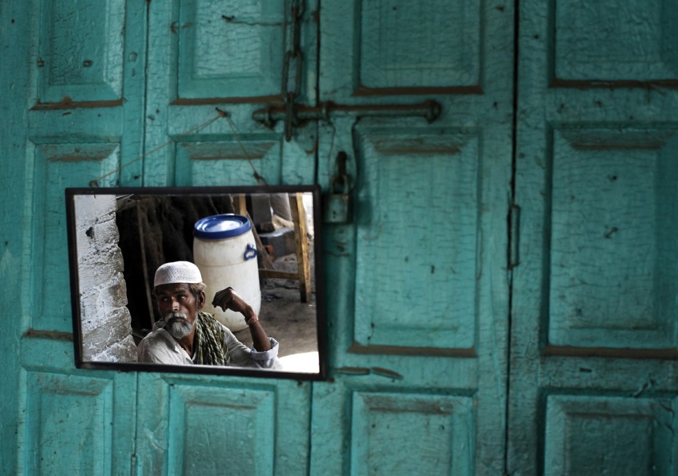 Amruddin Siddiqui is reflected in a mirror as he sits at a roadside in the old quarters in Delhi