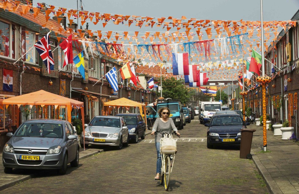 A woman rides her bicycle past orange decorated houses in the Vlierboomstraat