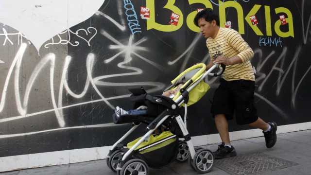 A man pushes a pram in front of a Bankia bank logo in Madrid