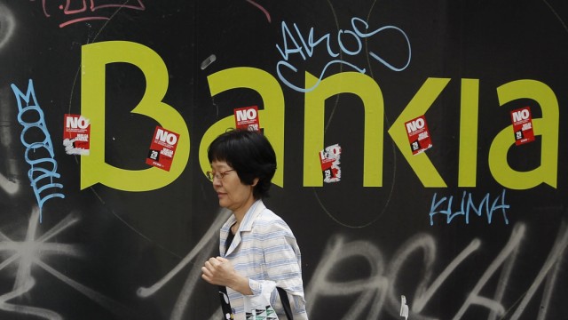 A woman walks past a defaced logo of nationalized lender Bankia in Madrid