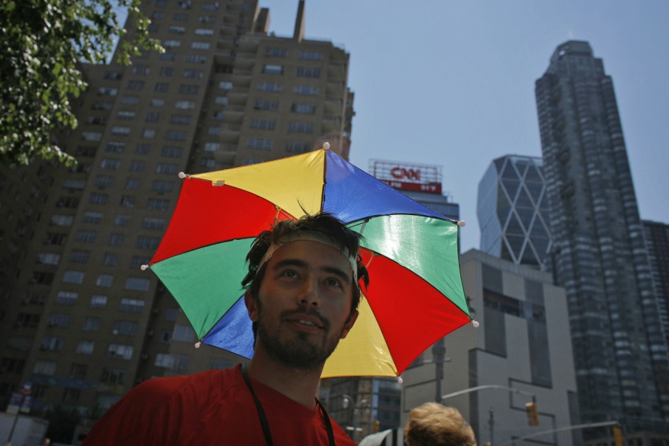 A man covers himself from the sun with an umbrella attached to his head walking around Central Park in New York