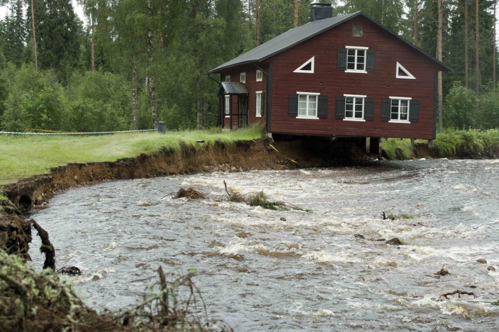 A house, with its foundation washed away, hangs over a rain-swollen creek at Nyhammar in Dalarna