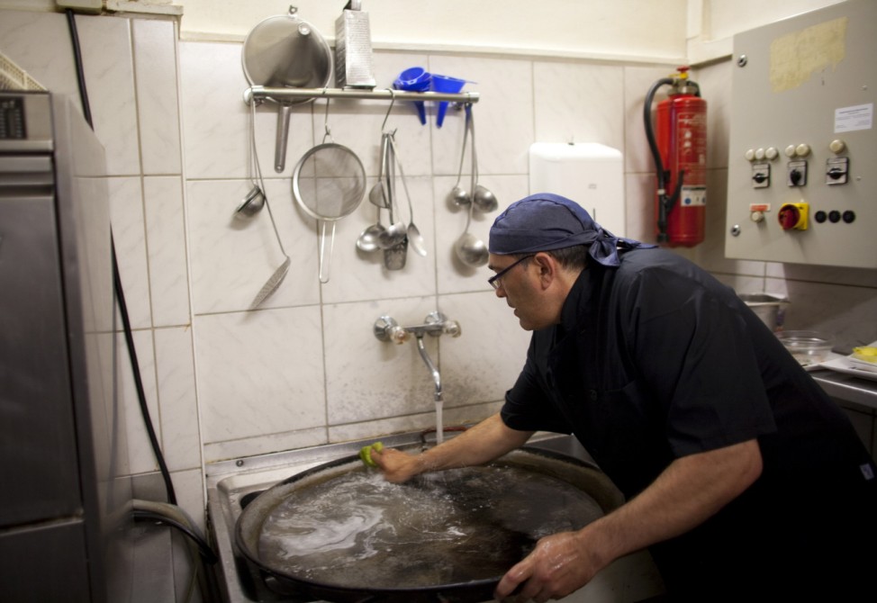 Jose Manuel Abel washes a paella pan while working as a kitchen assistant in Munich