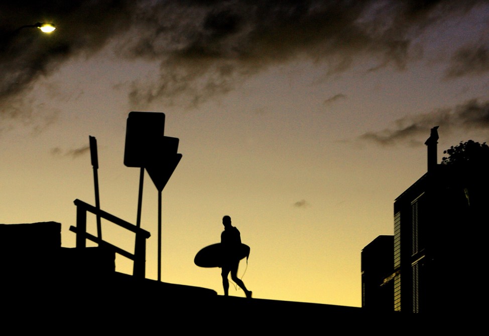 A surfer crosses the road with his board at sunset above Sydney's Bondi Beach