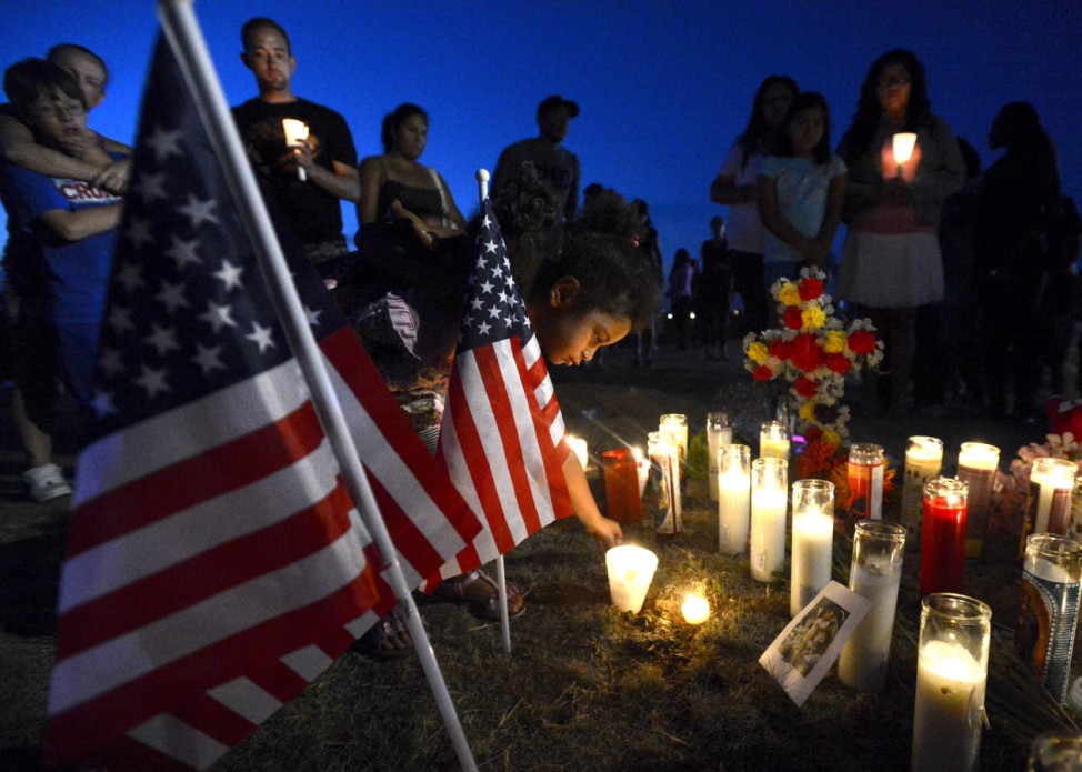 Young places a candle by an American flag during a vigil for victims behind a theater where a gunman open fire in Aurora, Colorado