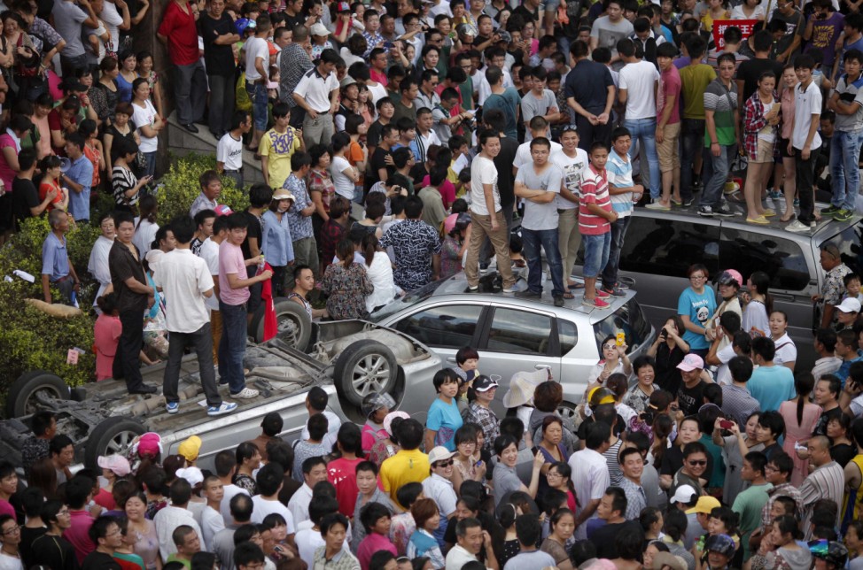 Local residents stand on smashed cars as they occupy the local government building during a protest against an industrial waste pipeline under construction in Qidong