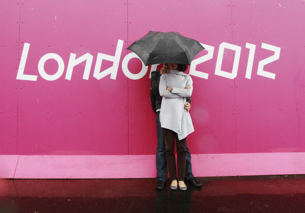 A couple shelter from the rain at the Riverbank Arena at the London 2012 Olympic Games in the Olympic Park in east London