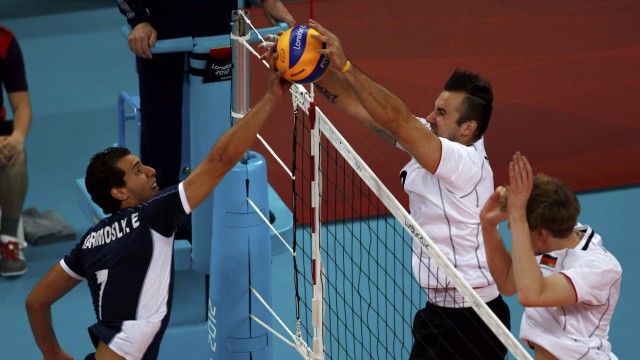 Tunisia's Elyes Karamosly spikes the ball against Germany's Gyorgy Grozer and Bjorn Andrae during their men's Group B volleyball match at Earls Court during the London 2012 Olympic Games