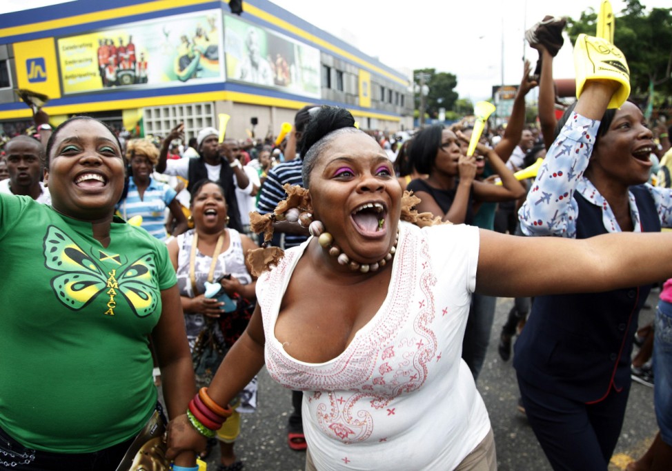 Jamaicans react while watching Jamaica's Campbell-Brown and Fraser-Pryce compete in the women's 200m final during the London 2012 Olympic Games in Half Way Tree
