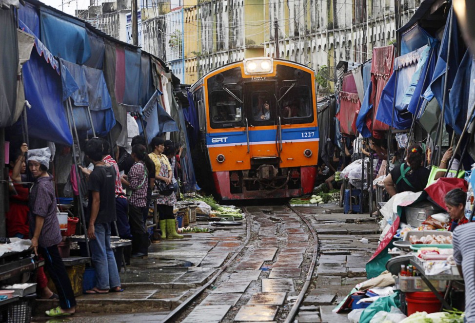 Thai vegetable market vendors pull back awnings and their produce off a railway track to allow a cross-country train to dissect through the middle of the town of Maeklong