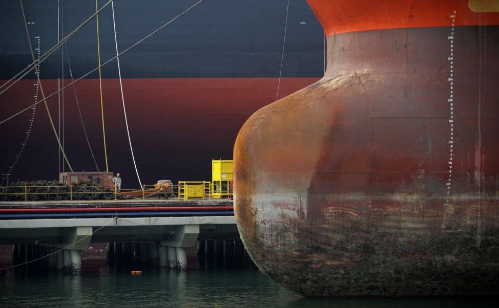 A worker is dwarfed by vessels berthed at a pier in Keppel Shipyard in Singapore