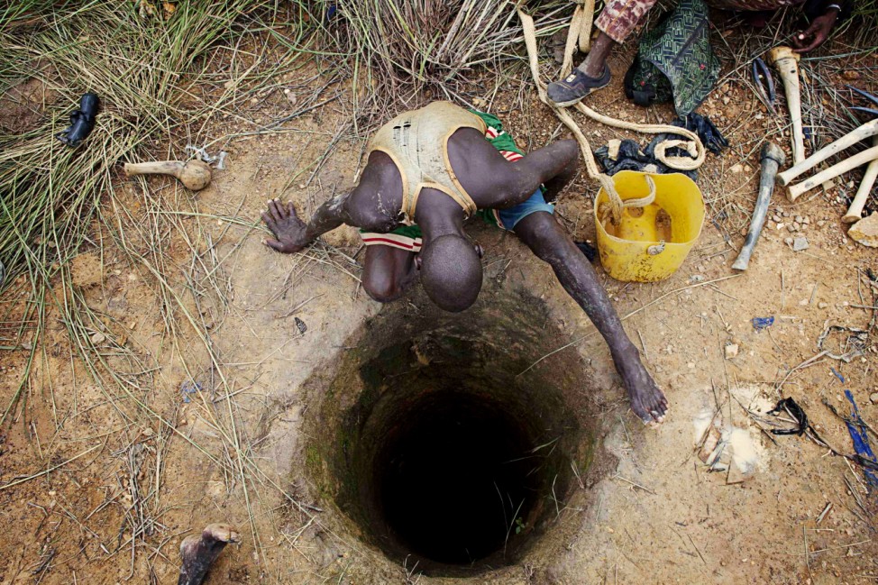 An artisanal gold miner peers into a small-scale mine where his colleague is working in Kalana