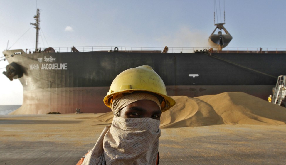 A worker stands against the backdrop of a cargo ship being loaded with wheat at Mundra port in Gujarat